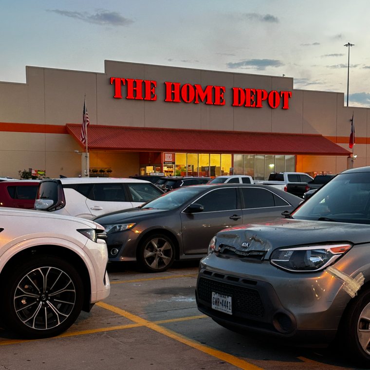 The Home Depot storefront at dusk with the red sign lit, seen across a full parking lot.