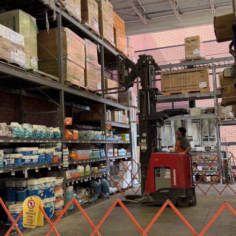 A Home Depot associate on a reach truck lifting toward the top shelf in a closed aisle.