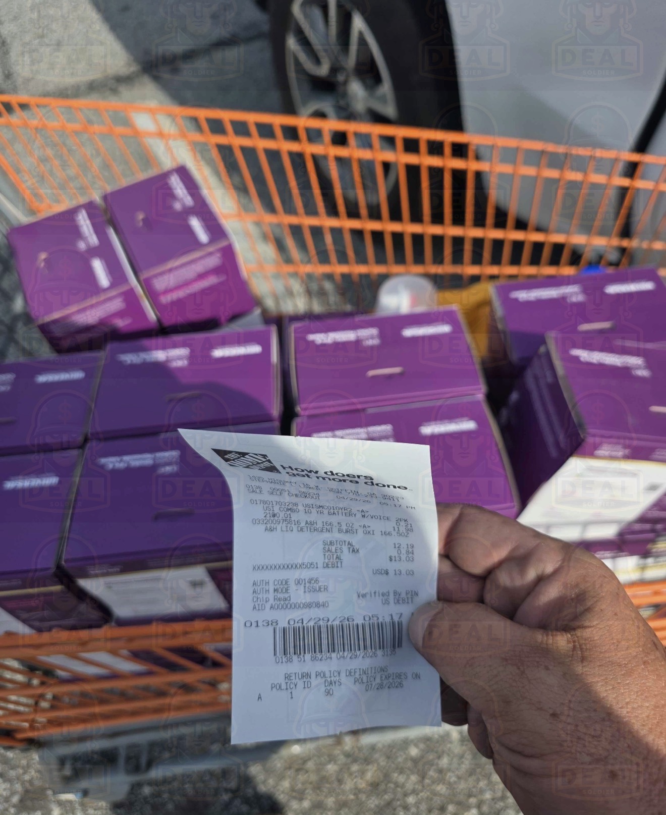 Home Depot orange shopping cart in the parking lot loaded with 21 purple Universal Security Instruments combination smoke and carbon monoxide detector two-packs, with a Home Depot receipt held over the boxes confirming the penny haul.
