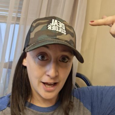 Deal Soldier member in a camo Deal Soldier trucker cap pointing at the logo