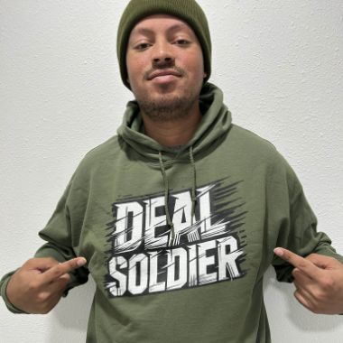 Deal Soldier member in an olive Deal Soldier hoodie and beanie pointing at the chest logo