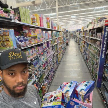 Deal Soldier member in a Deal Soldier cap with a cart of toy clearance in a Walmart aisle
